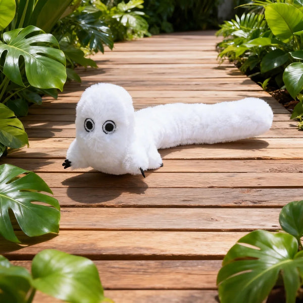 A white anime witch hat plush toy lying on a wooden deck surrounded by green foliage.