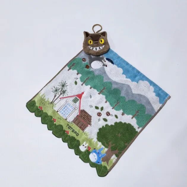 A plush toy of a brown hippopotamus with large eyes is displayed on a green felt mat featuring a landscape.