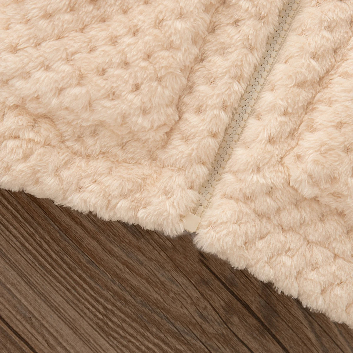 A close-up of a beige plush hooded winter jacket fabric resting on a wooden surface.