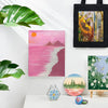 A collection of art prints featuring vibrant pink and green landscapes, a yellow portrait, and a dark fabric tote bag.