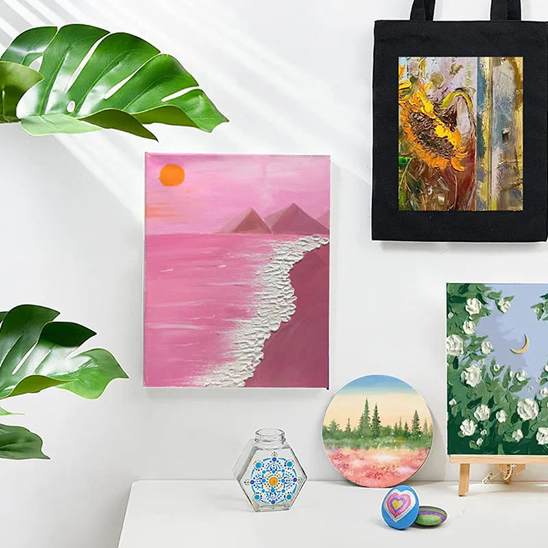 A collection of art prints featuring vibrant pink and green landscapes, a yellow portrait, and a dark fabric tote bag.