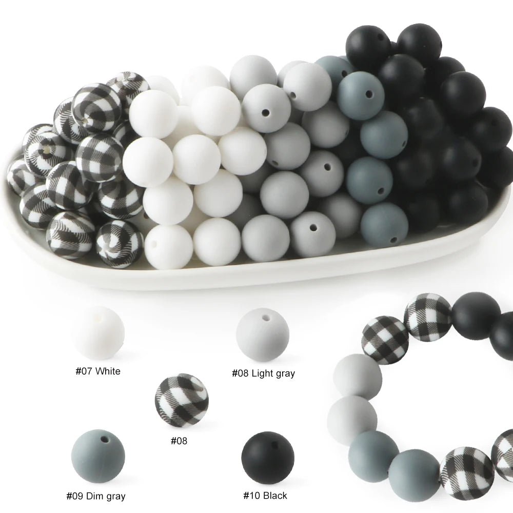 A collection of soft food-grade silicone beads in various colors including white, gray, and black, displayed on a white plate