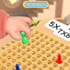 A hand is drawing cards from a multiplication board game featuring a yellow calculator keypad and various colored cards.