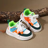 A pair of orange and white casual sneakers with green accents rests on a brown wooden log.