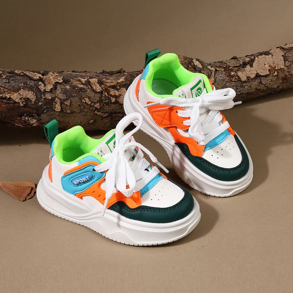 A pair of orange and white casual sneakers with green accents rests on a brown wooden log.