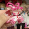 A hand holds a pink and white patterned doll fashion set with large eyes.