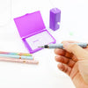 A hand holds an electric diamond painting pen kit with a silver body and purple box in the background.