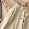 A beige long sleeve shirt with a small brown bear embroidery on the chest, shown flat lay.