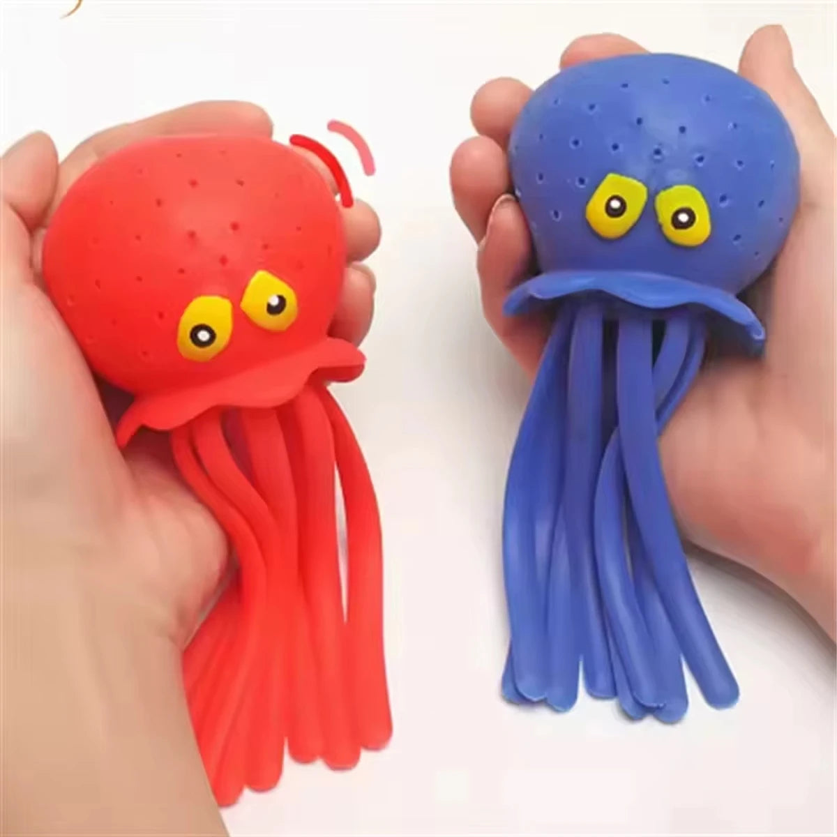 A bright red squeeze water octopus bath toy with tentacles is held in a hand next to a blue squeeze water octopus.