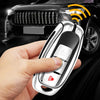 A hand holds a silver key case cover designed for Infiniti models, with a car in the background.