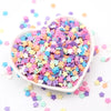 A pile of colorful polymer clay sprinkles in various pastel shades scattered on a white surface.