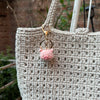A light beige crocheted handbag featuring a pink animal keychain.