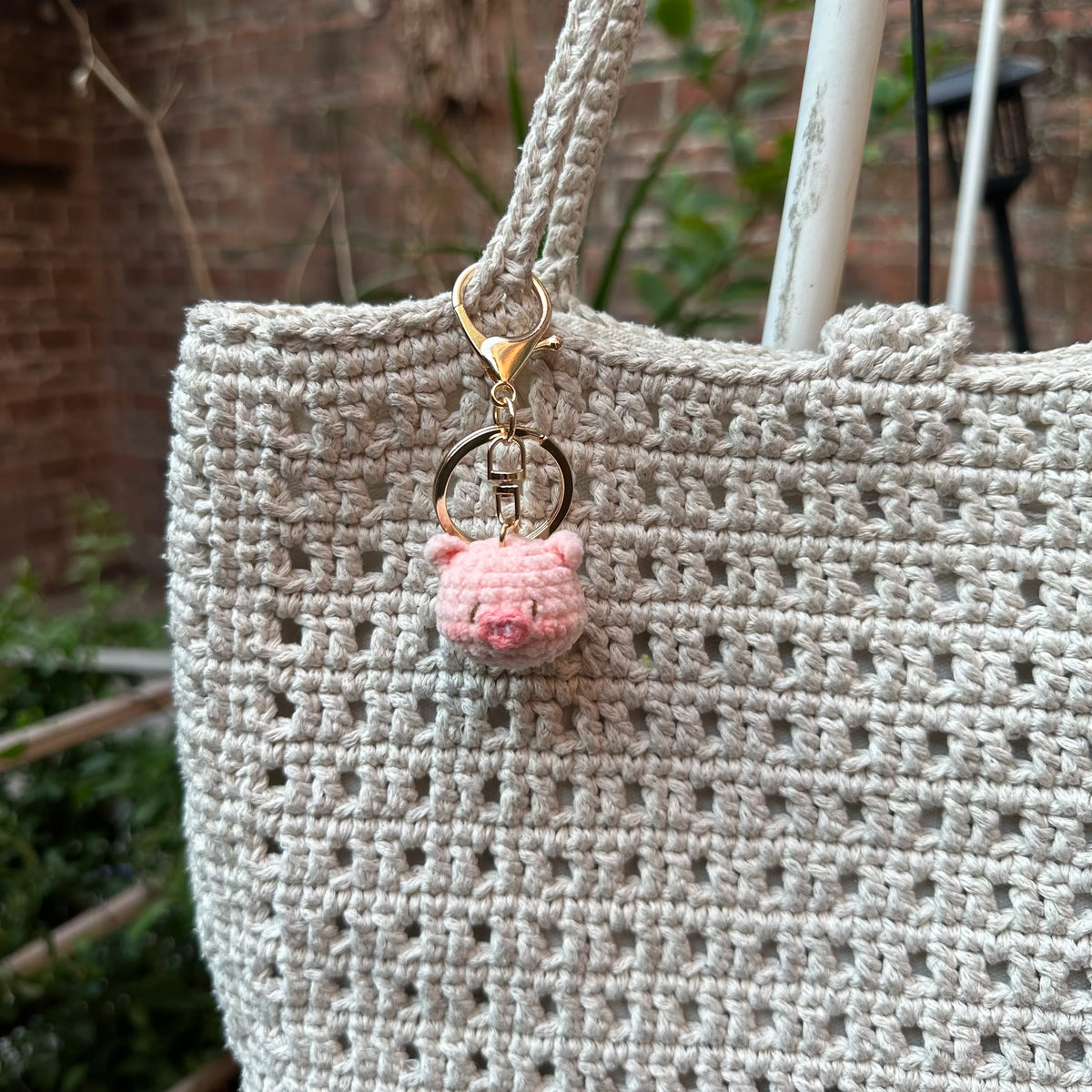 A light beige crocheted handbag featuring a pink animal keychain.