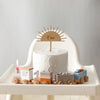 A white cake decorated with a golden sun topper sits on a wooden train set featuring numbered cars.
