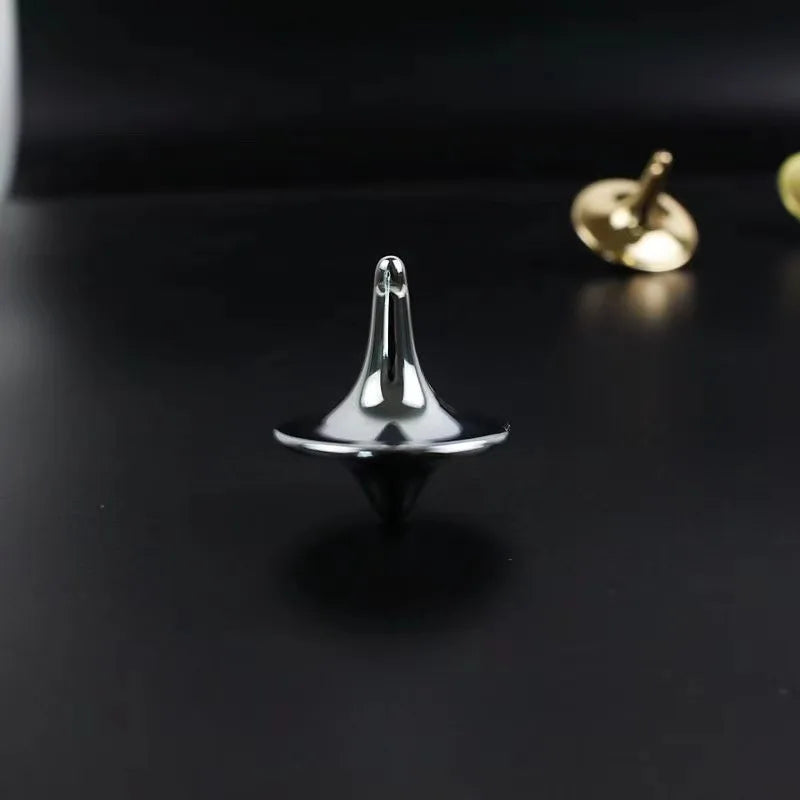 A silver metal fidget spinner resting on a dark surface next to a gold-colored object.