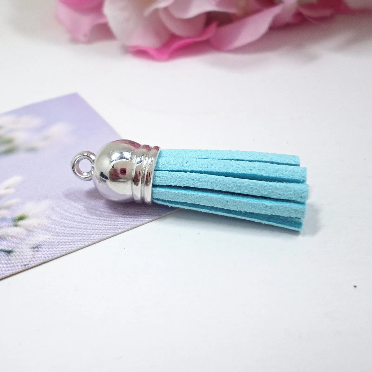 A bundle of light blue velvet tassels with silver metal findings resting on a purple card.