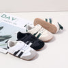 A collection of baby first walkers soft sole shoes in beige, black, and white with green accents.
