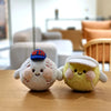 Two fluffy plush charms resembling sports balls, one blue and white with text, and one yellow, resting on a wooden surface.