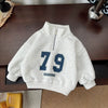 A light gray college sports sweatshirt with the number 79 embroidered on the chest, displayed on a dark wooden surface.