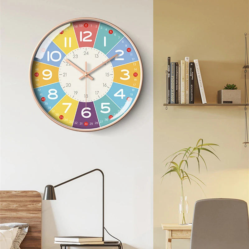 A round analog teaching clock with a colorful face showing numbers 1 through 12 and days of the week, mounted on a light wall