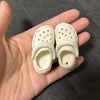 Pair of white fashion slippers with perforated detailing shown in a person's hand.
