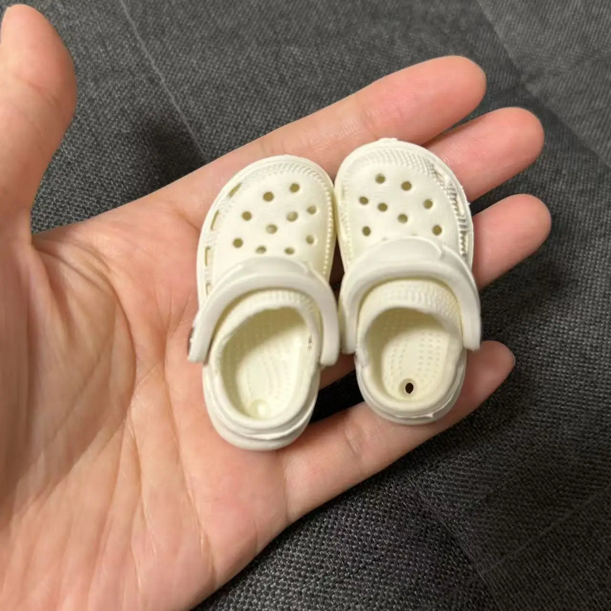 Pair of white fashion slippers with perforated detailing shown in a person's hand.