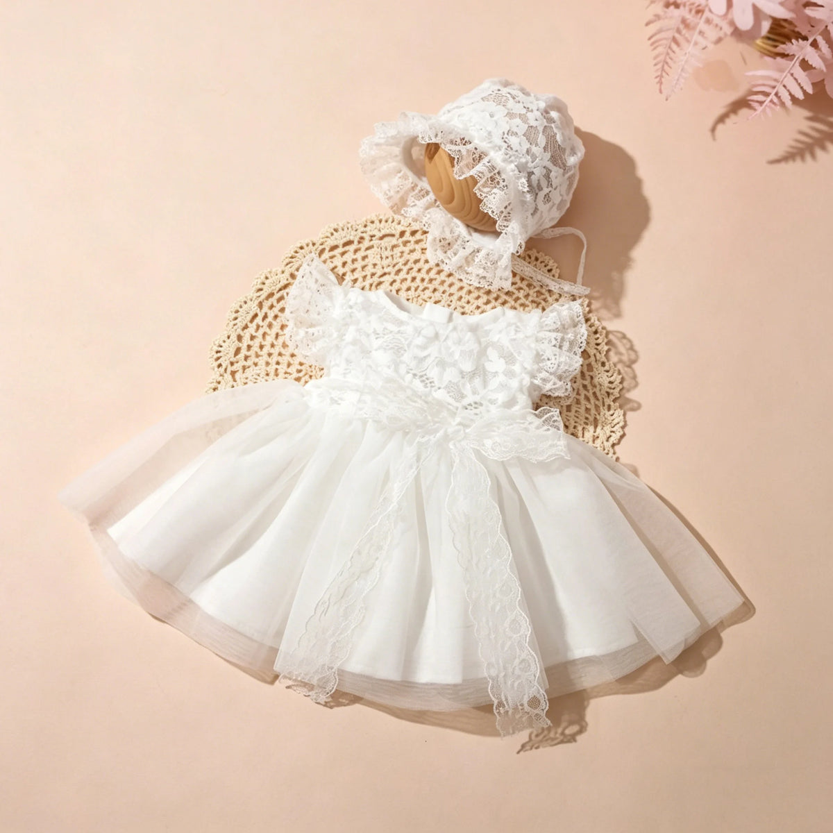A white lace tulle dress for a newborn baby girl is displayed with a matching lace hat on a neutral background.