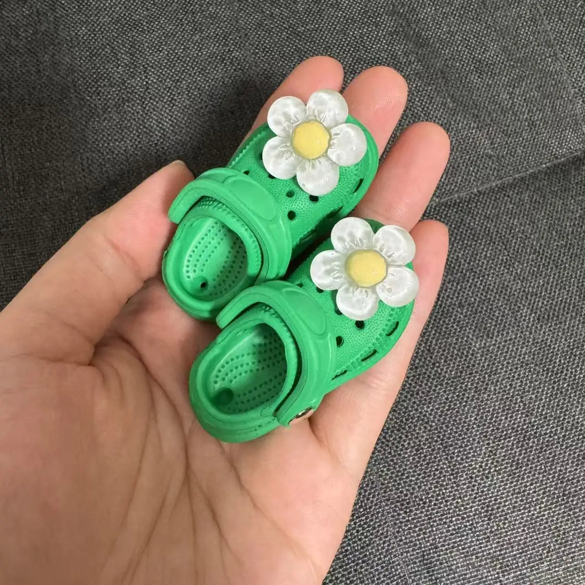 A pair of bright green fashion slippers with white and yellow floral accents are held in a hand.