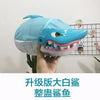 A hand holds a light blue shark-shaped toy with an open mouth showing teeth, used as a prank board game.