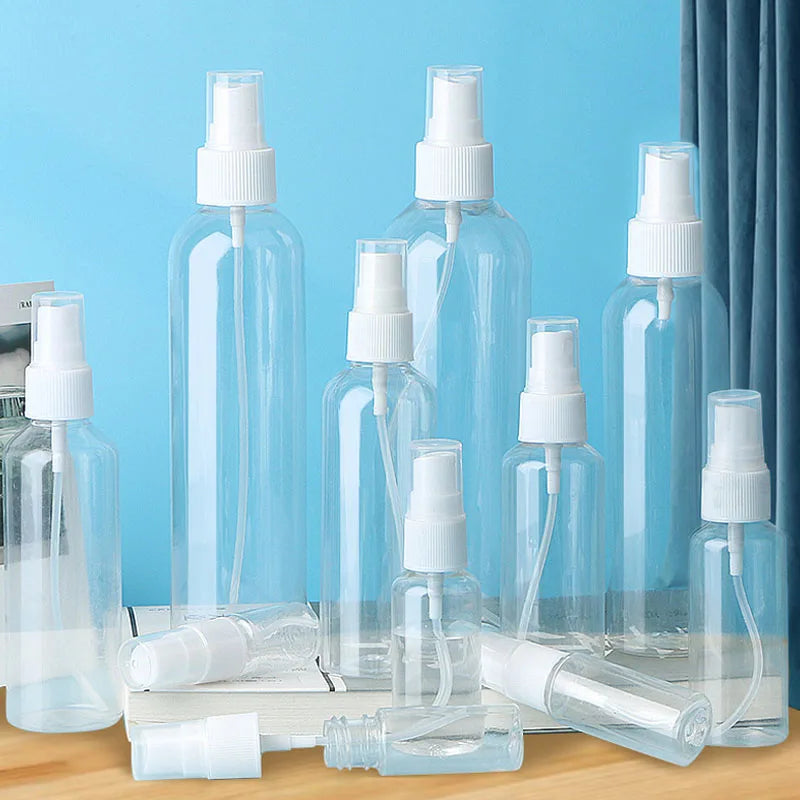A collection of three clear glass refillable travel spray bottles with fine mist pumps arranged on a wooden surface.