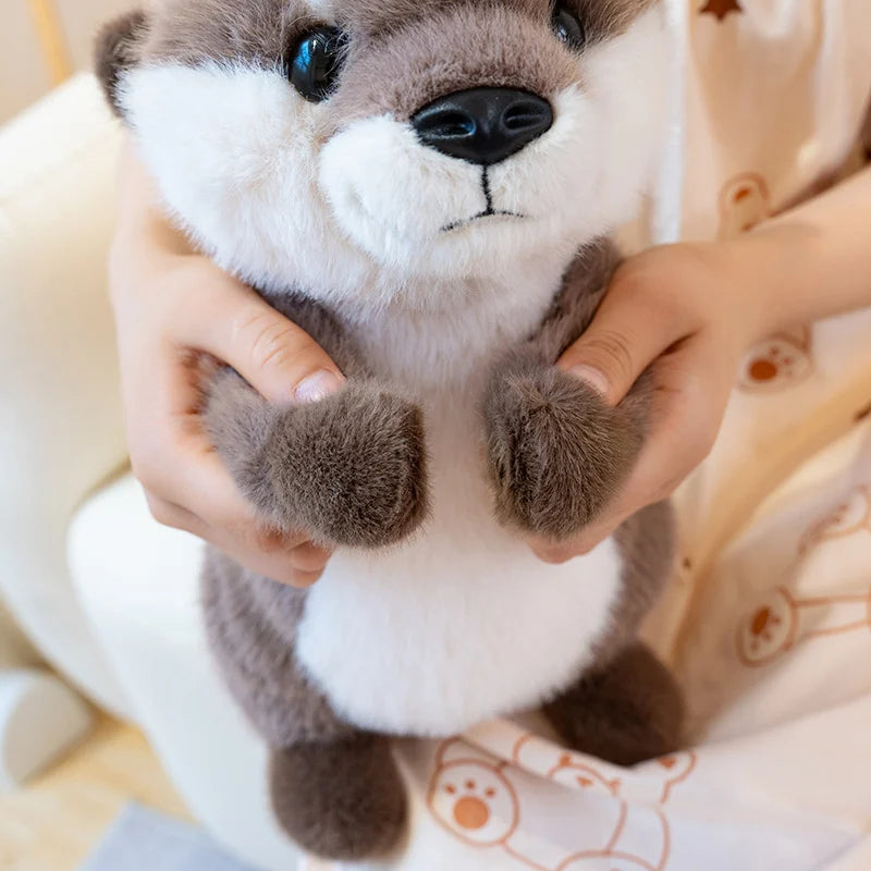 A person is holding a gray and white magnetic otter plush toy.