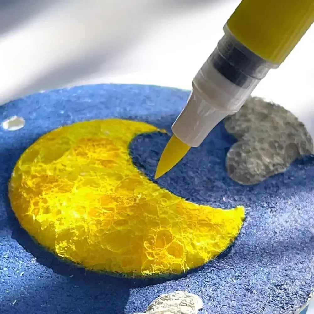 A yellow crescent shape is being painted onto a blue surface with a yellow marker pen.