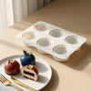 A white silicone mold with multiple circular cavities is shown next to a plate of baked fruit desserts.