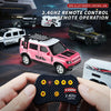 A hand holds a remote control for a pink off-road RC car, with other toy vehicles visible in the background.