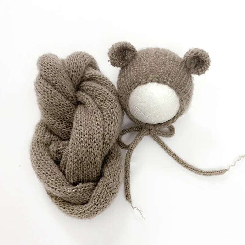 A knitted bear hat and wrap set in a taupe color with a white pom-pom.