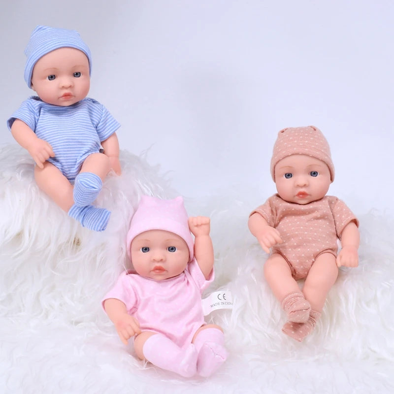 A set of three realistic soft vinyl reborn baby dolls wearing blue, pink, and tan outfits lying on white fluffy material.