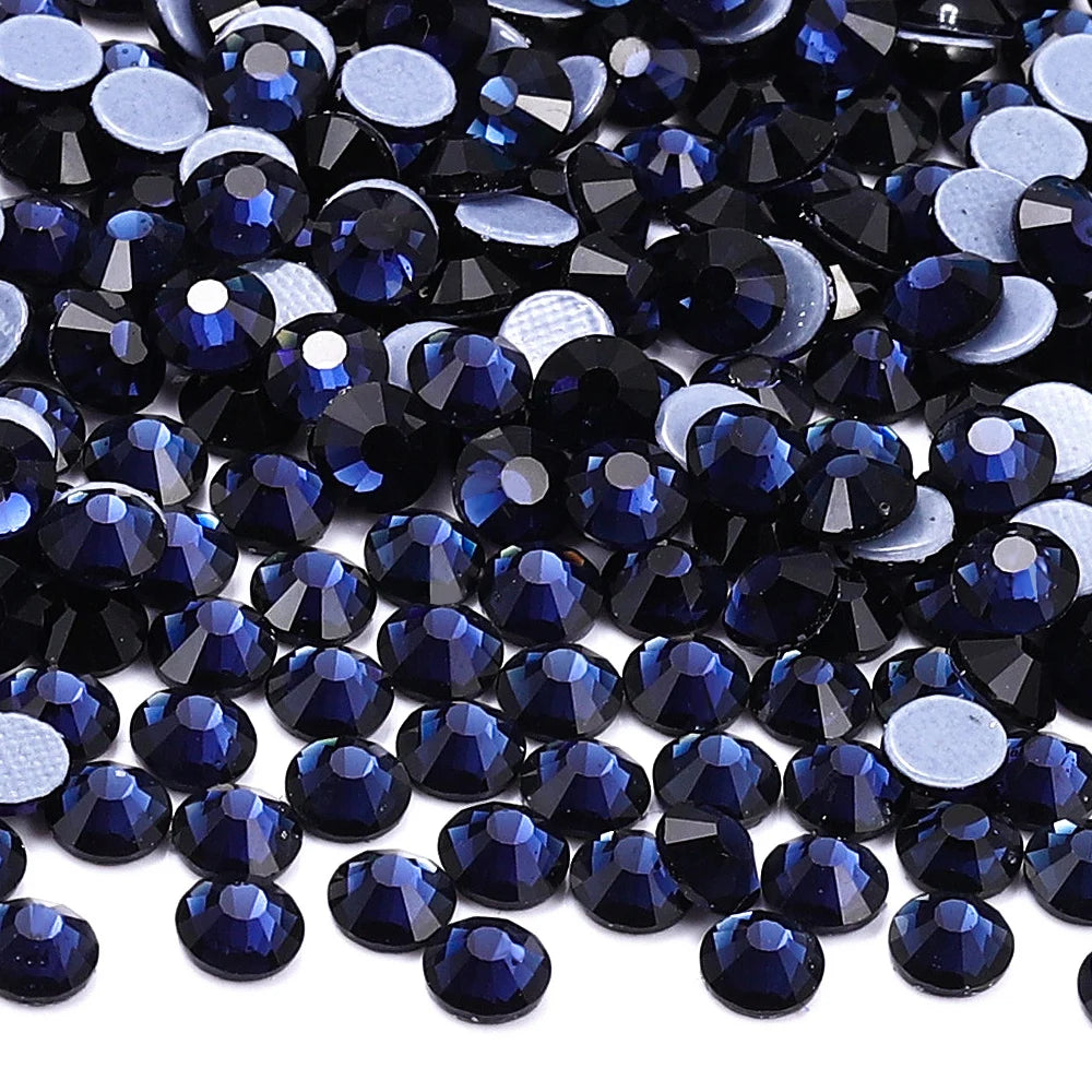 A close-up view of dark blue and black glass crystal rhinestones scattered on a white background.