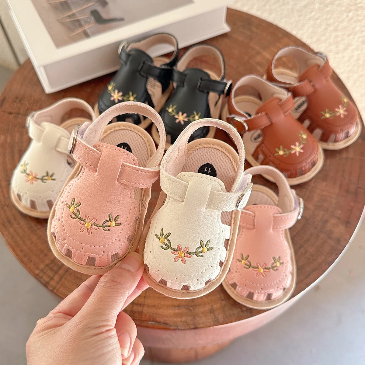Ein Paar rosa und beige Babysandalen für den Sommer, präsentiert auf einer Holzoberfläche.