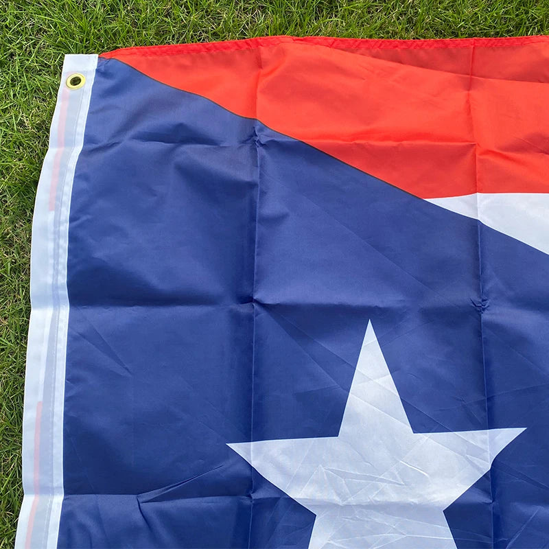 A folded Puerto Rico national flag banner showing the red and blue design with a white star on a green lawn.