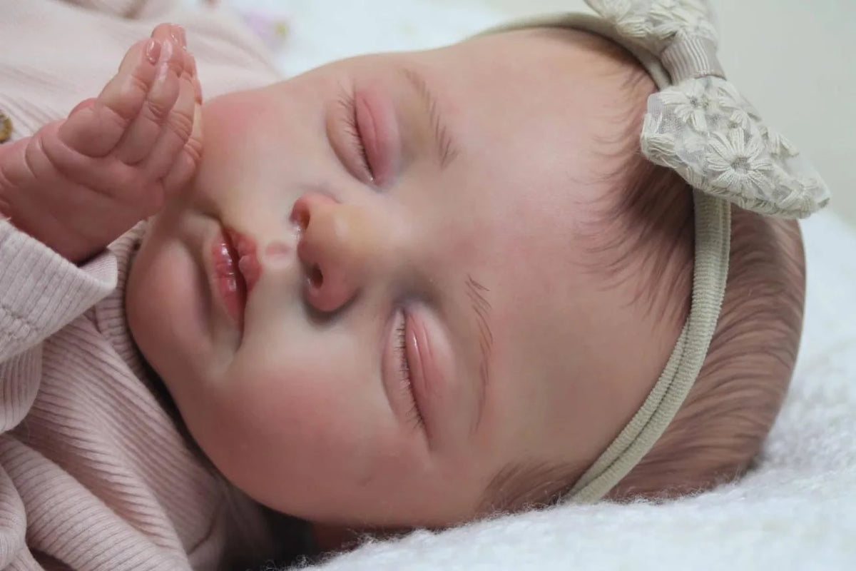A close-up of a lifelike 19-inch reborn baby doll with soft cloth body sleeping peacefully.