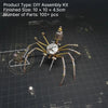 A finished steampunk metal spider assembly kit with multiple legs and a detailed body, displayed on a dark grid background.