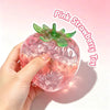 A hand holds a pink strawberry squishy stress ball with green leaves, highlighting its texture and vibrant color.