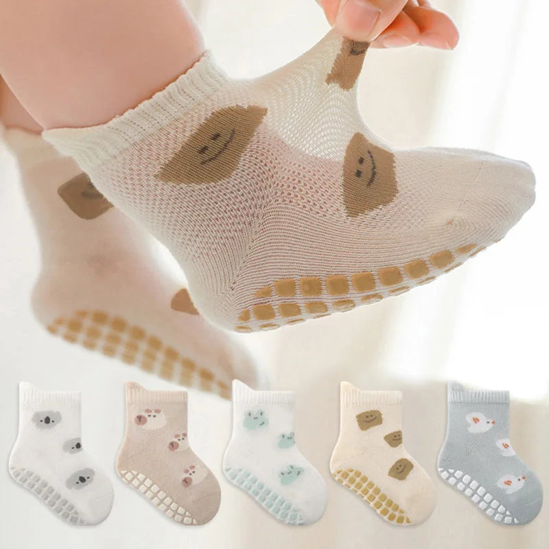 A close-up of a pair of beige knitted socks with light brown cartoon animal designs being held by a hand.