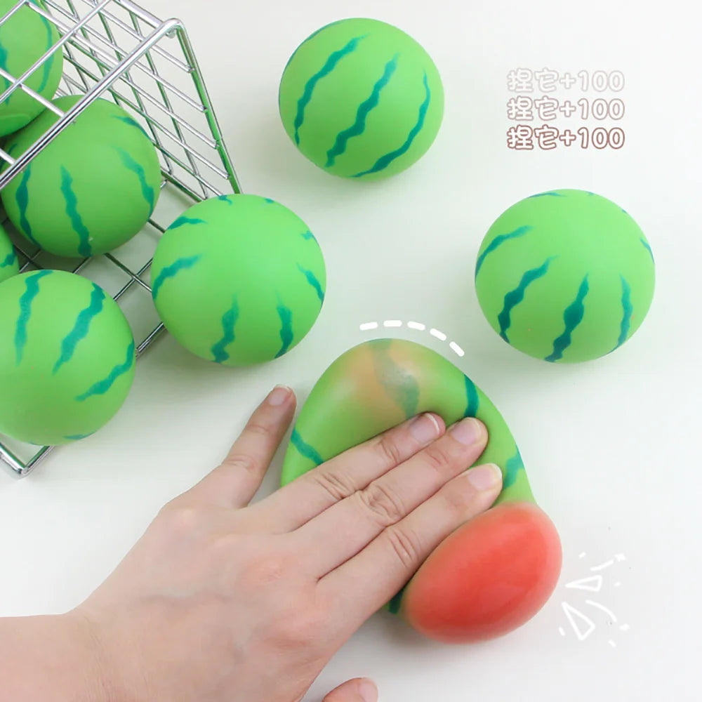 Eine Hand drückt ein wassermelonenförmiges Stressabbau-Spielzeug, mit anderen grünen Spielzeugen und einem Metallgitter sicht