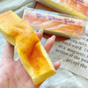 A hand holds a yellow butter stick squishy toy with orange and yellow coloring, next to packaged versions.
