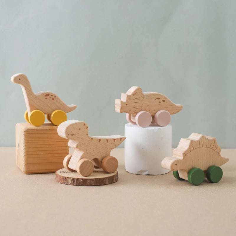 A set of wooden dinosaur teether toys in natural wood tones and light pink, resting on a beige surface.