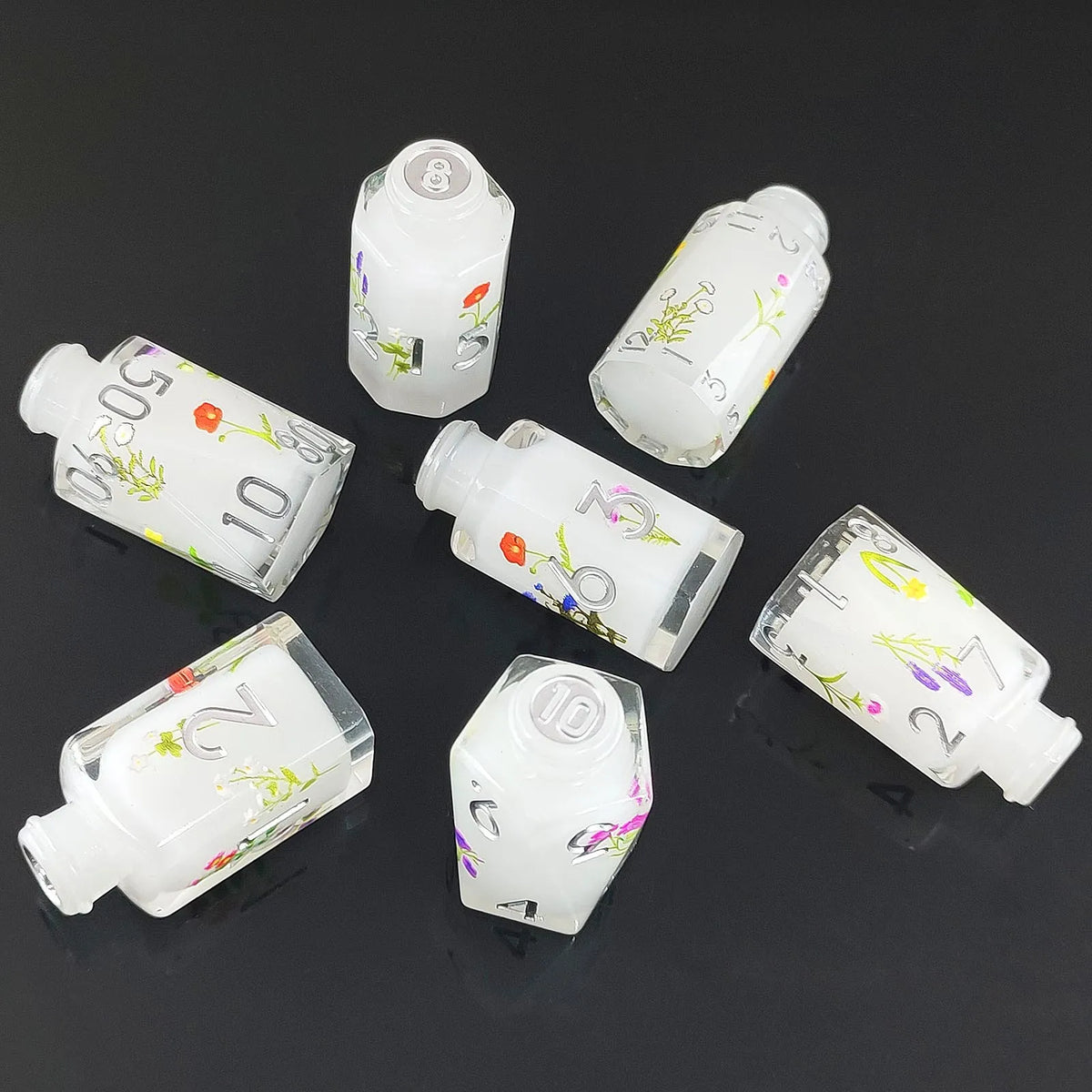 A set of seven white floral resin potion bottles shaped like polyhedral dice, arranged on a dark surface.