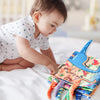 A baby is interacting with a colorful dinosaur-themed soft cloth book for sensory play.