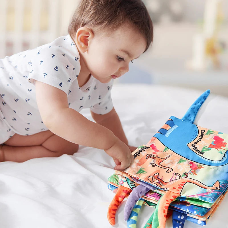 A baby is interacting with a colorful dinosaur-themed soft cloth book for sensory play.