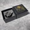 A black box containing a revolver-shaped metal dice set for RPG games with a gold emblem on the lid.
